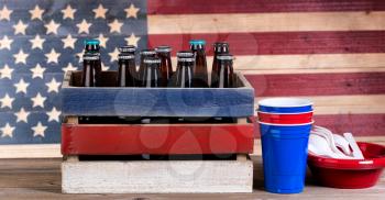 Crate of beer and party stuff for Fourth of July celebration with vintage wooden USA flag in background.