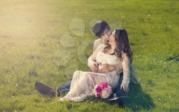 Expecting mom and dad lying in tall grassy field holding each other. Haze light effect applied to image.    