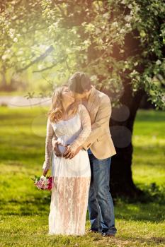 Expecting mom and dad kissing under flowering tree. Haze light effect applied to image.    