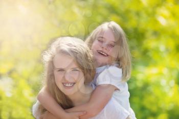 Front forward view, with focus on face of older girl, of sisters sharing a close moment while outdoors. Light haze effect applied to image. 
