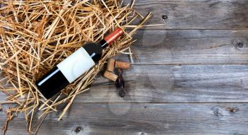 Overhead view of a red wine bottle on top of straw with vintage wine corkscrew and corks. 