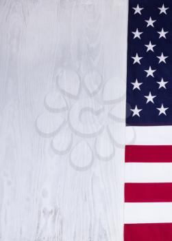 Folded cloth flag, right border, of United States of America on white wood in vertical format.