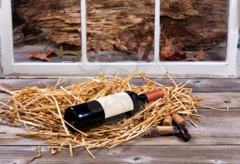 Bottle of wine on straw with old cork screw on rustic wood and window in background.