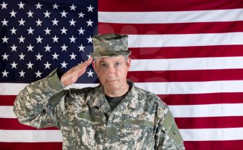 Veteran male soldier, facing forward, saluting with USA flag in background. 
