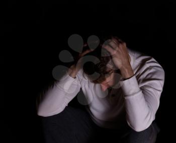 Depressed mature man holding head while looking down. Dark background. 