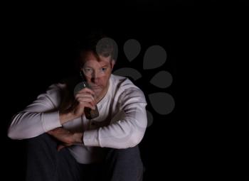 Depressed man holding bottle of beer against face while in thought. Dark background. 