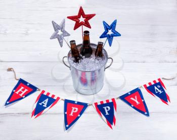Colorful stars, banner and a bucket of ice with bottled beer on rustic white wood. Fourth of July holiday concept for United States of America.  