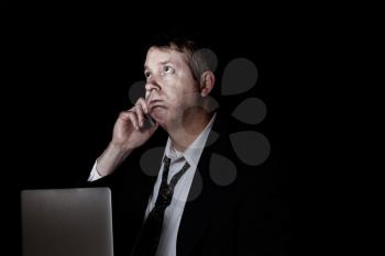 Side view of stressed business man on cell phone while working.  Dark background with light on face.  