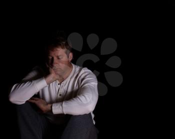 Depressed mature man, eyes closed, and resting head in right hand. Dark background with copy space available. 