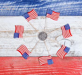 Small USA flags forming circle around American liberty dollar coin on red, white and blue rustic boards. Fourth of July holiday concept for United States of America.  