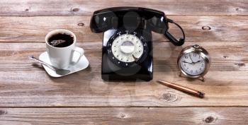 Vintage desktop with antique telephone, pen, clock and coffee on rustic wooden boards.