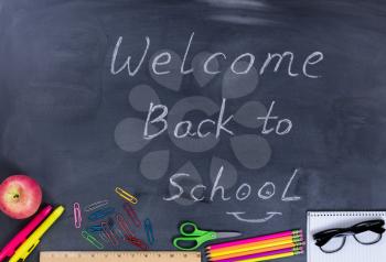 Back to school concept with supplies on chalkboard with written message to welcome students.