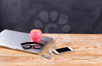 Back to school concept with modern technology consisting of laptop, cell phone, thumb drive and reading glasses in front of erased black chalkboard. 