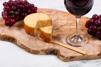 Close up of sliced gourmet cheese with red wine and grapes on wooden server in background. Selective focus on front of cheese wedge.  