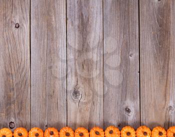 Overhead view of seasonal autumn pumpkin decorations, lower border, on rustic wooden boards. 