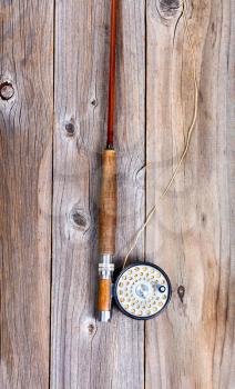 Top view of antique fly rod and reel on rustic wooden boards in vertical layout. 