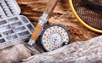 Close up view of antique fly rod, reel, landing net and lure container in stone and drift wood setting. 

