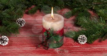 Close up of a burning candle with fir branches and pine cones on rustic red wooden boards for Christmas concept. 