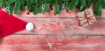 Rustic red wooden background for Christmas concept with fir branches, candy canes, red berries, Santa cap, gift box and pine cones. Overhead view with copy space.