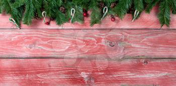Rustic red wooden background for Christmas concept with fir branches, candy canes, red berries and pine cones. Overhead view with copy space