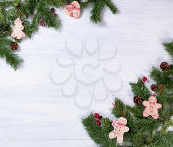 White wooden background with fir branches, cookies, pine cones and red berries in corners for Christmas concept. 
