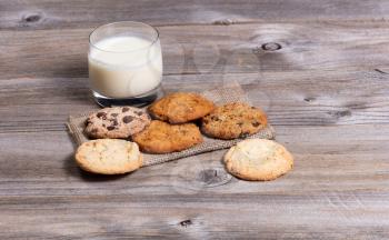 Front view of a variety of freshly baked cookies on a napkin with a glass milk. 