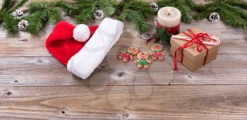 Rustic wooden boards with Christmas holiday candle, cookies, gift box, Santa cap and evergreen branches.   