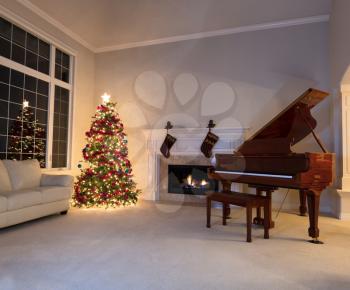 Bright Christmas tree in living room with burning fireplace and grand piano during night time.