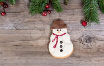 Frosted Snowman cookie on rustic wood with evergreen fir top border.