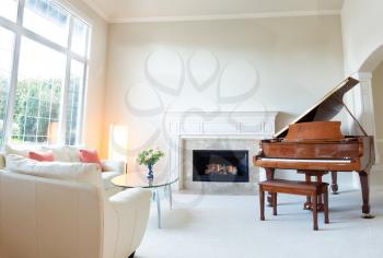 Bright day light coming into living room with burning fireplace, grand piano and white leather sofa. 