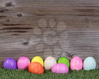 Colorful Easter egg decorations lying on grass with rustic wood in background. 