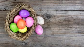 Colorful Easter eggs in bird nest on rustic wooden boards. Flat view layout with copy space.  