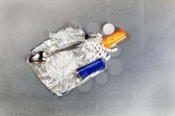 Flat view of crushed painkiller pills with open bottle, aluminum foil, spoon, lighter and syringe. Opioid epidemic concept.