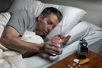 Mature man holding medicine and a glass of water while trying to fall asleep. Insomnia concept. 