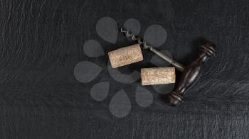 Overhead view of antique wine corkscrew and used corks on black slate 