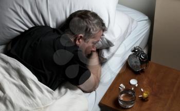 Mature man staring at alarm clock while trying to fall asleep. Insomnia concept. 