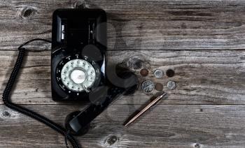 Flat layout of vintage telephone, pen and coins on rustic wood with lighting effects applied. 