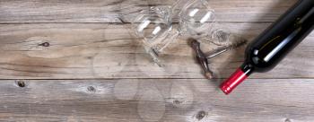 Flat view of a bottle of red wine, antique corkscrew, and drinking glasses on rustic wooden boards