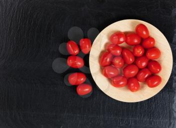 Overhead view of fresh cherry tomatoes on bamboo plate with black slate