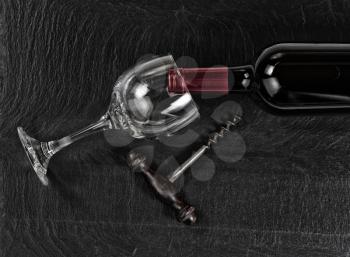 Overhead view of antique wine corkscrew, red wine bottle, and drinking glass on black slate 