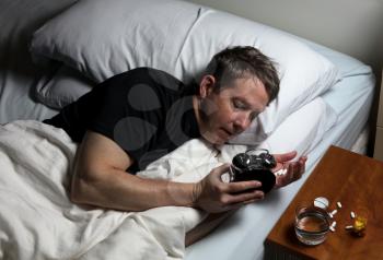 Mature man checking time on alarm clock while preparing to take medicine. Insomnia concept. 