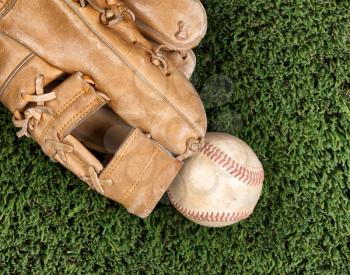 Flat view of old baseball mitt and used ball and on grass surface