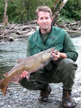 Mature man holding large salmon fish with river and woods in background