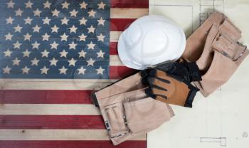 Labor Day background with USA rustic wooden flag, drawing blue prints and used industrial tools plus utility belt 