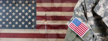 Military uniform with United States of America patch flag and burning sparkler in background on rustic wooden flag. July 4th holiday concept. 