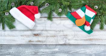 Top border of Christmas tree fir branches, Santa and elf hats on rustic wood in flat lay format