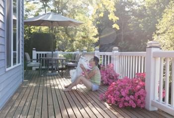 Mature woman holding her family dog while outdoors on home deck during bright summer morning with lens flare 