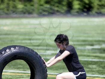 Close up of teen age girl pushing large tire on sports field to build strength 