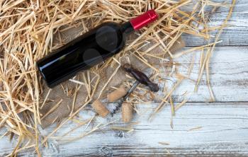 Overhead view of a red wine bottle plus corkscrew with straw and burlap on white rustic boards 