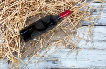 Overhead view of a red wine bottle with straw and burlap on white rustic boards 